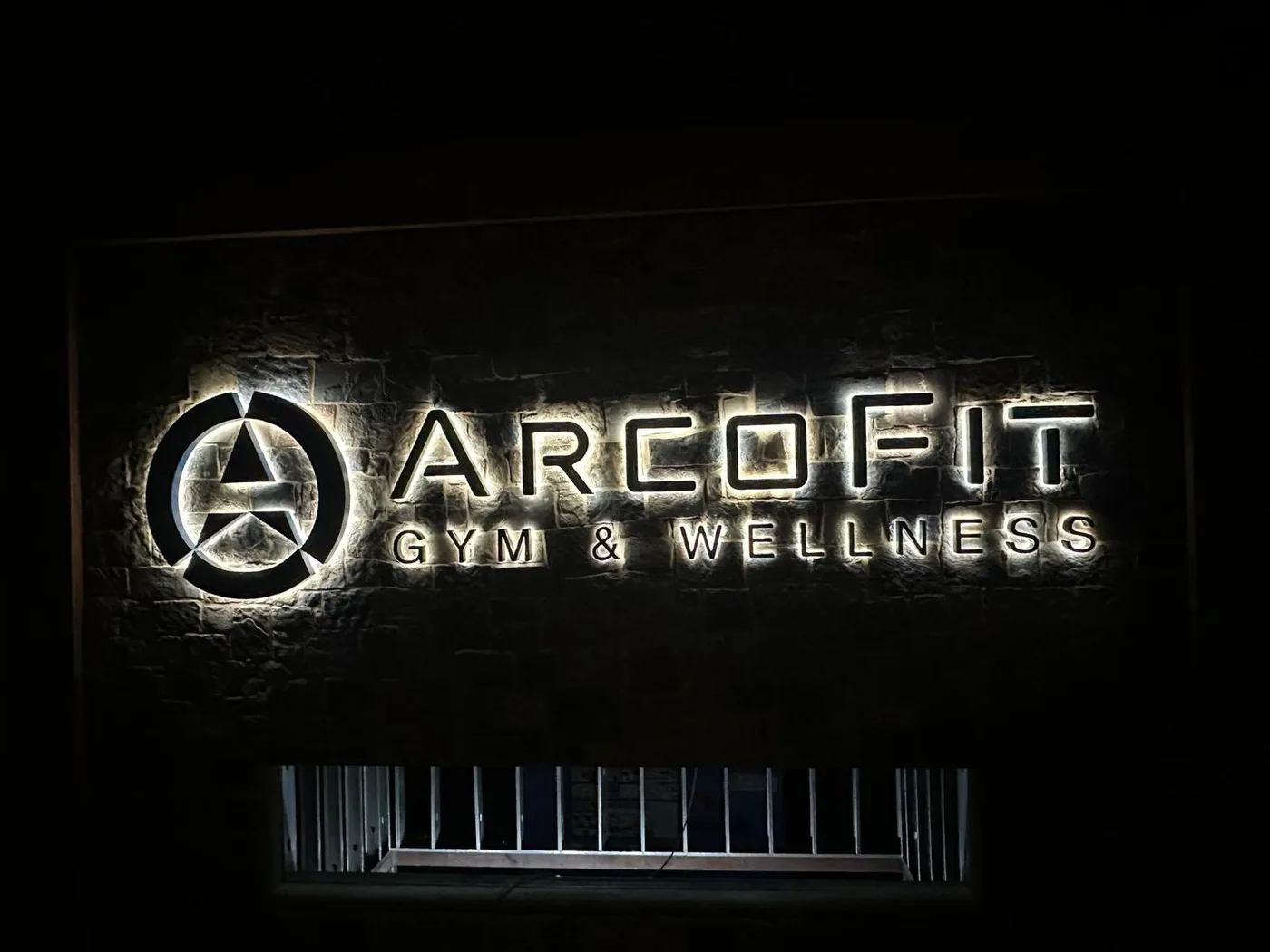 Halo-lit dimensional storefront sign for ArcoFit Gym and Wellness on a stone facade in Houston, Texas, illuminated at night