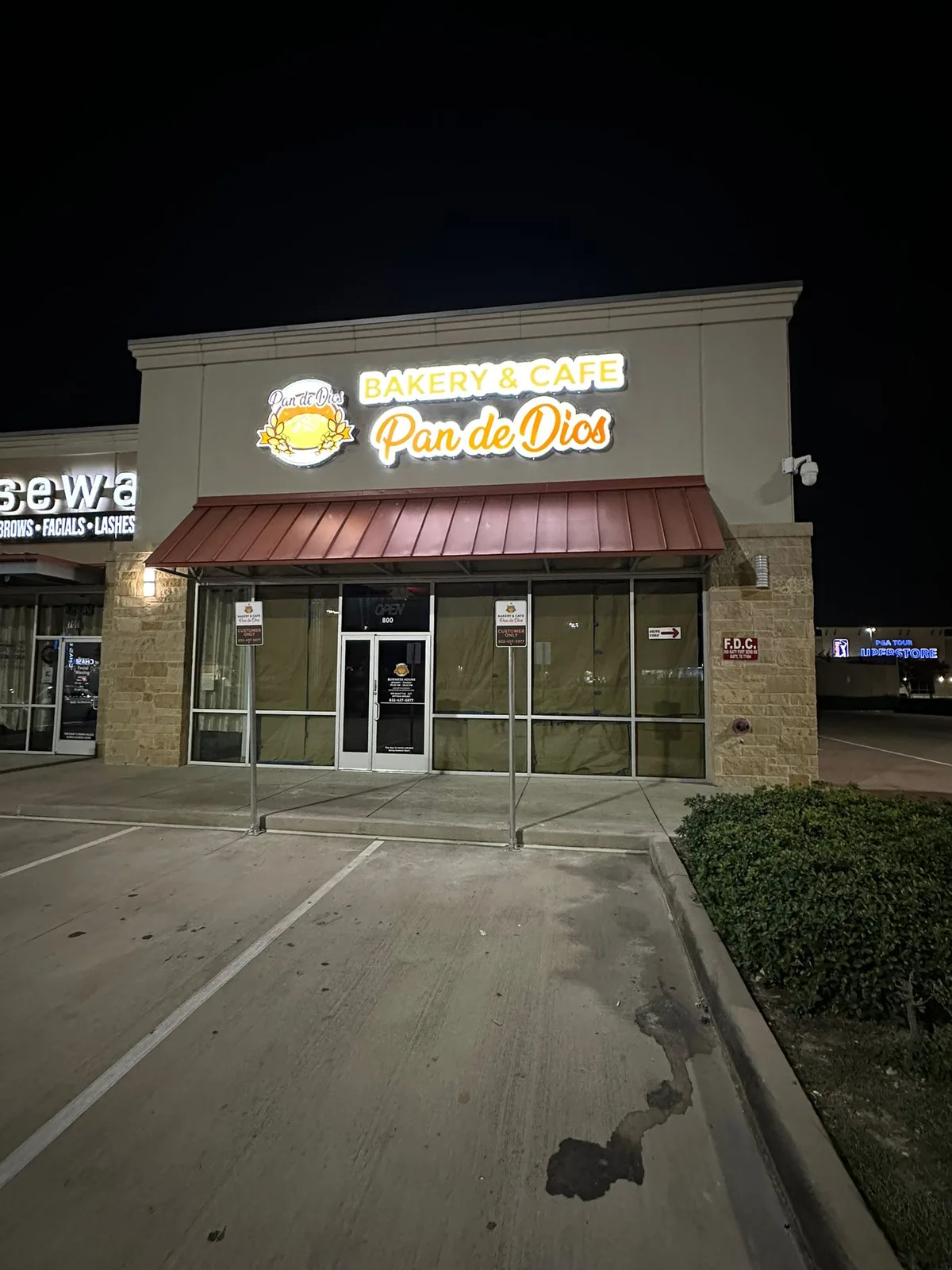 Illuminated cabinet storefront sign for Pan de Dios Bakery and Cafe in Houston, Texas, glowing at night